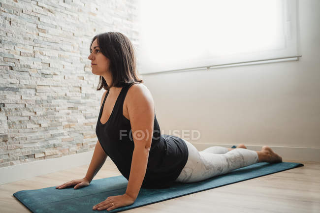 Junge brünette Frau macht Yoga auf Matte zu Hause — Stockfoto