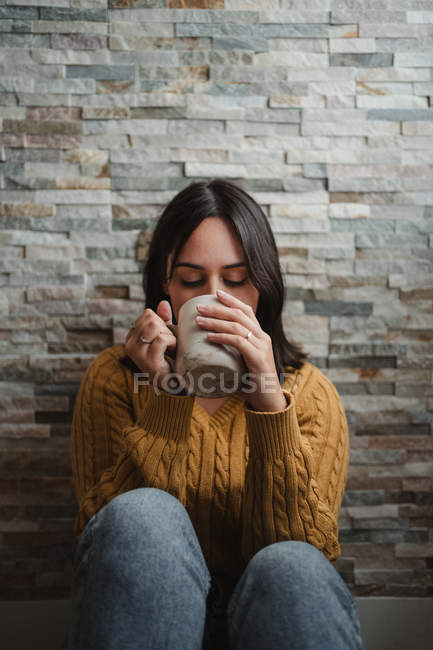 Mujer en suéter amarillo acogedor bebiendo té caliente en casa - foto de stock