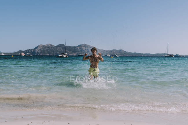 Человек в купальнике, бегущий в воде по берегу моря — стоковое фото