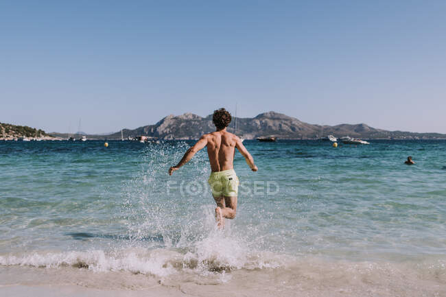 Man in swimsuit running in water on seashore — Stock Photo