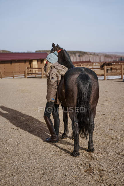Warm gekleidete Frau mit braunem Pferd bei Heu auf Bauernhof — Stockfoto