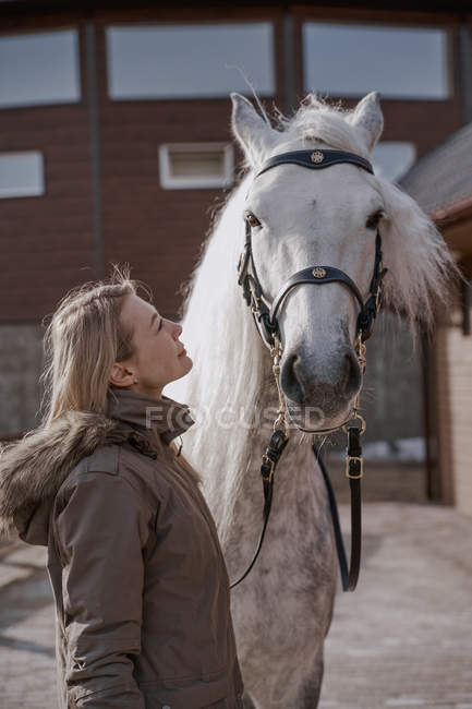 Warm dressed woman with gray horse outside in farm yard — Stock Photo