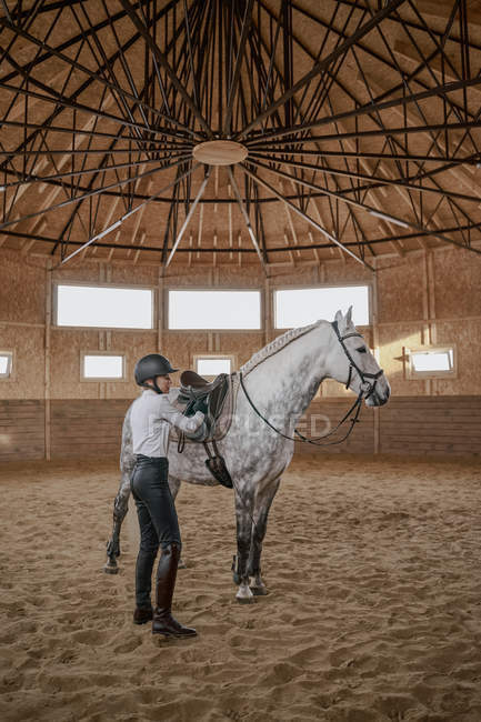 Horsewoman with dapple gray horse with long fluffy tail walking around light big arena — Stock Photo
