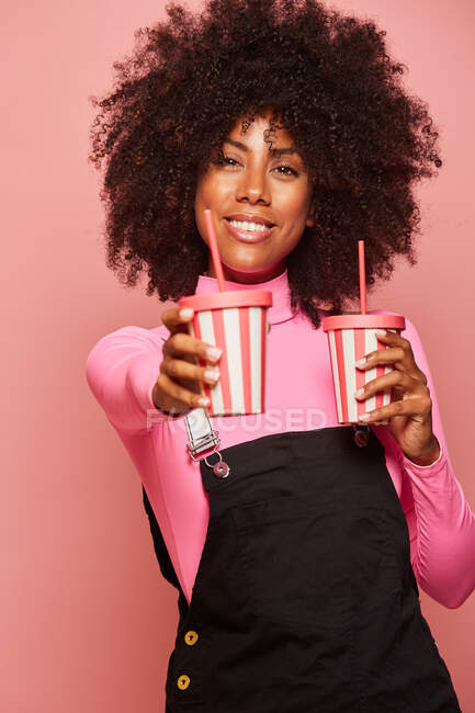 Happy black woman with disposable cup of drink standing against pink background — Stock Photo