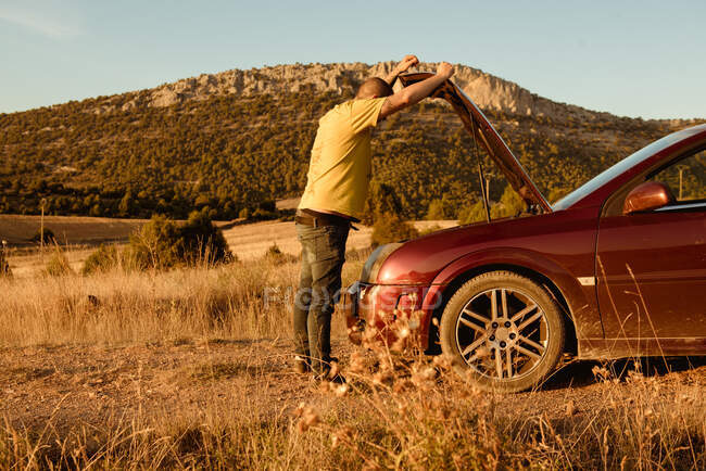 Side view of unrecognizable adult man opening hood looking at engine of broken car after accident in countryside — Stock Photo