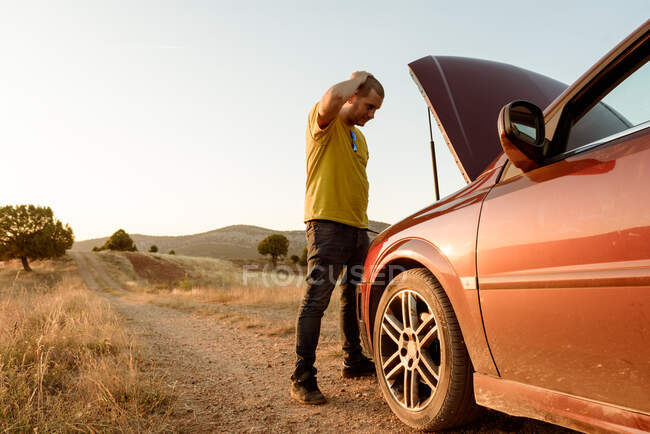 Homem examinando carro quebrado no campo — Fotografia de Stock