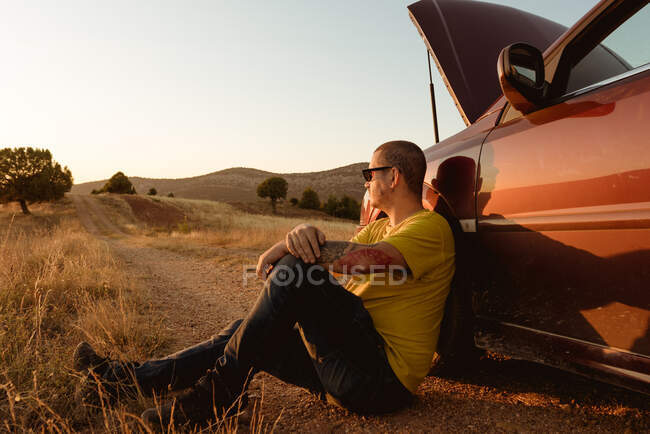 Чоловік спирається на зламаний автомобіль у сільській місцевості — стокове фото