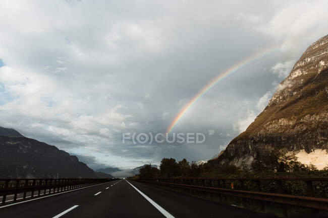 Autostrada solitaria tra montagne e cielo con arcobaleno — Foto stock