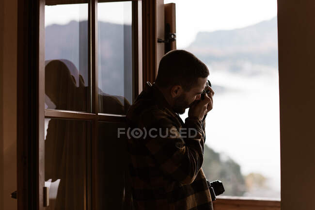 Fotografía masculina en ropa casual tomando fotos de la ventana abierta - foto de stock