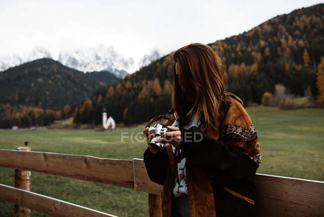 Donna con macchina fotografica in piedi vicino alla chiesa in montagna — Foto stock