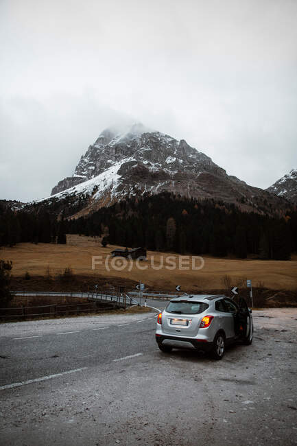 Lonely road with car on roadside among pine forest near big clif — Stock Photo