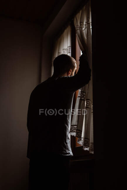 Hombre en ropa casual de pie junto a una ventana - foto de stock