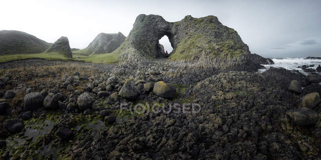 Vista lateral da fêmea em roupa quente em pé na borda do penhasco dentro da caverna no porto da Irlanda do Norte olhando para o mar — Fotografia de Stock