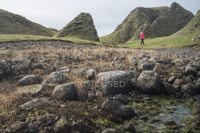 Anonyme Frau genießt die atemberaubende malerische Landschaft Nordirlands während ihrer Reise, während sie in der Nähe des schnellen flachen Flusses wandert, der zu den Gewässern der felsigen Küste fließt — Stockfoto