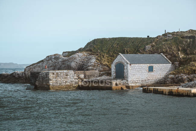 Ancient stone building with doors on picturesque pier of Ballintoy harbour on rocks background — Stock Photo