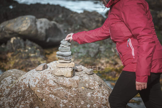 Vista lateral de la mujer anónima de la cosecha en la chaqueta de construcción de piedra de pequeñas rocas durante el viaje por Irlanda del Norte - foto de stock