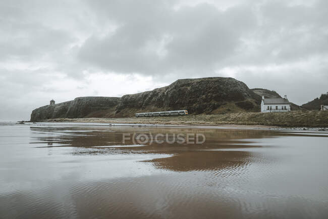 Paysage pittoresque avec Temple Mussenden situé sur une falaise de pierre à la côte d'Irlande du Nord et vagues de mer orageuses se précipitant contre des roches avec un ciel gris nuageux en arrière-plan — Photo de stock