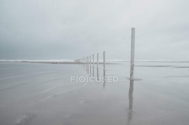 Clean sea water rippling near sandy coast against evening sky in countryside with row of wooden stick — Stock Photo