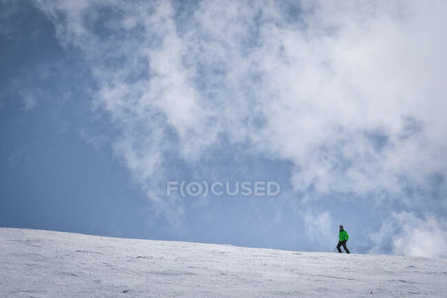 Joven de cuerpo completo en ropa verde y gafas de sol montando esquís en la ladera nevada de la montaña en el soleado día de invierno en el resort - foto de stock