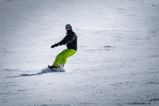 Unrecognizable person in outwear and headphones riding snowboard on snowy mountain slope on resort — Stock Photo