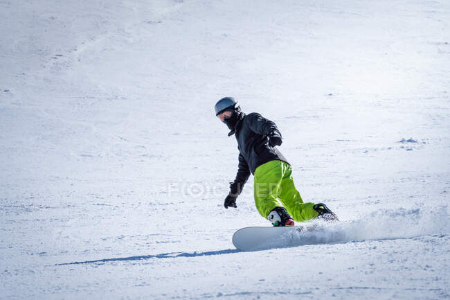 Unrecognizable person in outwear and headphones riding snowboard on snowy mountain slope on resort — Stock Photo