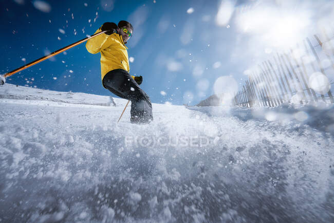 Joven de cuerpo completo en ropa interior amarilla y gafas de sol montando esquís en la ladera nevada de la montaña en el soleado día de invierno en el resort - foto de stock