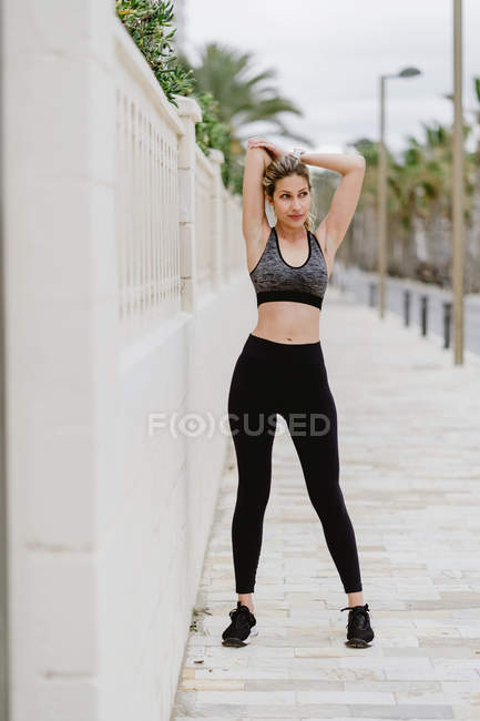Mujer deportiva motivada en desgaste activo estirando los brazos y mirando hacia otro lado - foto de stock