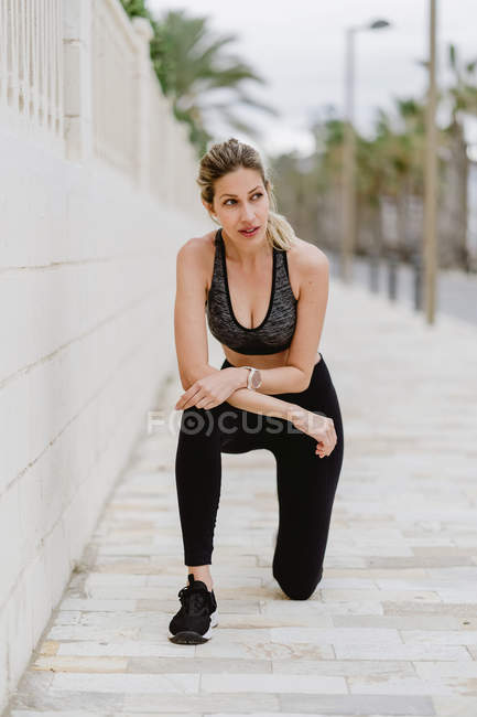 Contenu jeune athlète féminine dans des vêtements de sport élégants penchant les mains sur les genoux pendant l'entraînement — Photo de stock