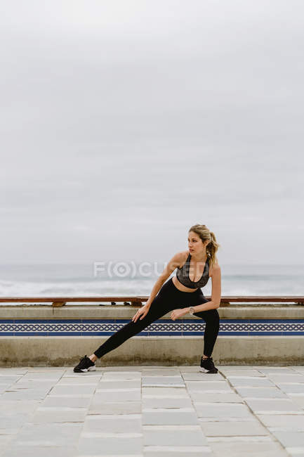 Мотивированная спортивная женщина в активном износе стоя и растягивая ноги, отводя взгляд — стоковое фото