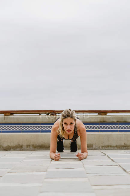 Konzentrierte Athletin in stylischer Aktivkleidung beim Planken am leeren Sandstrand am trüben Tag — Stockfoto