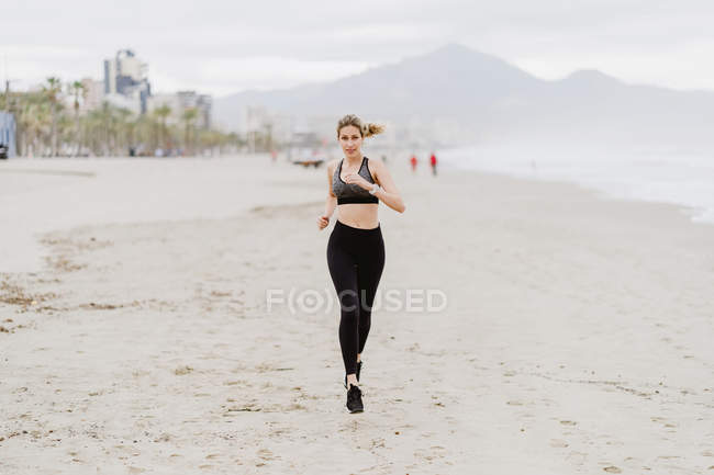Fitte Frau läuft bei trübem Wetter am tropischen, leeren Meeresufer entlang — Stockfoto