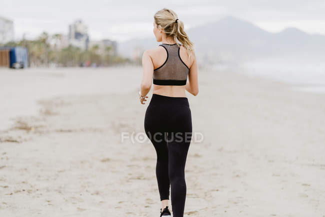 Visão traseira da mulher em forma correndo ao longo da costa tropical vazia em tempo nublado — Fotografia de Stock