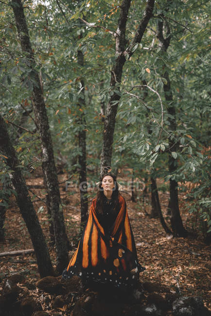 Jovem mulher em asas de borboleta capa dançando perto de árvores na floresta verde — Fotografia de Stock