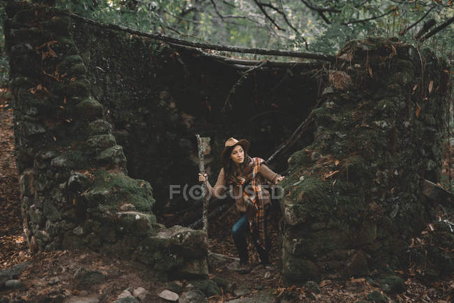 Mulher com pau de madeira explorando velhas ruínas na floresta verde na natureza — Fotografia de Stock