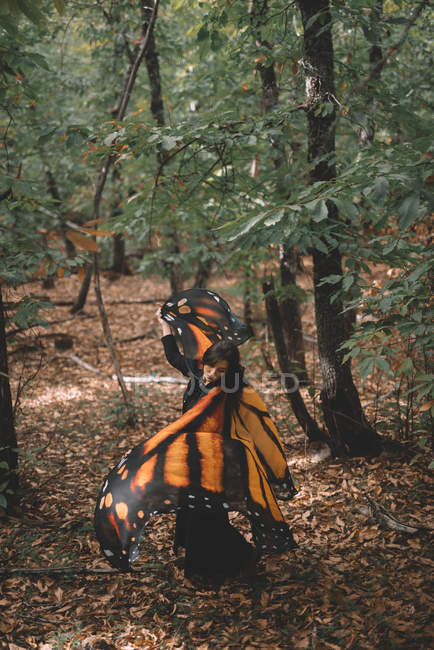Vue latérale de la jeune femme aux ailes de papillon cape dansant près des arbres dans la forêt verte — Photo de stock