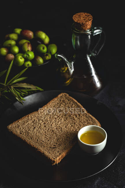 Aceite de oliva virgen extra español fresco con aceitunas y rama de olivo vieja sobre fondo oscuro Alimentación saludable Dieta mediterránea. Vegano. Vegetariano. Pan tostado - foto de stock