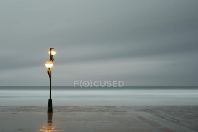 Quai en pierre de bloc vide et lanterne avec ciel gris et mer calme sur fond à Zarautz en Espagne — Photo de stock