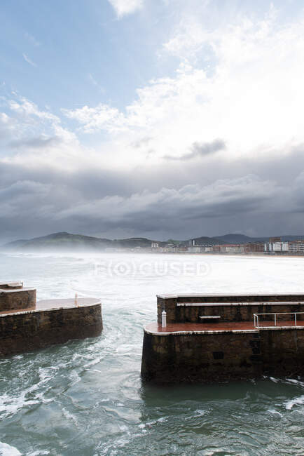 Roca rompeolas con el mar furioso en el tiempo nublado - foto de stock