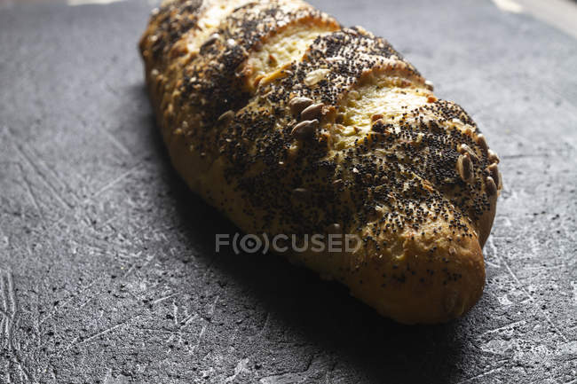 Rolo de pão fresco crocante ruivo com grãos e sementes de papoula em fundo cinza — Fotografia de Stock