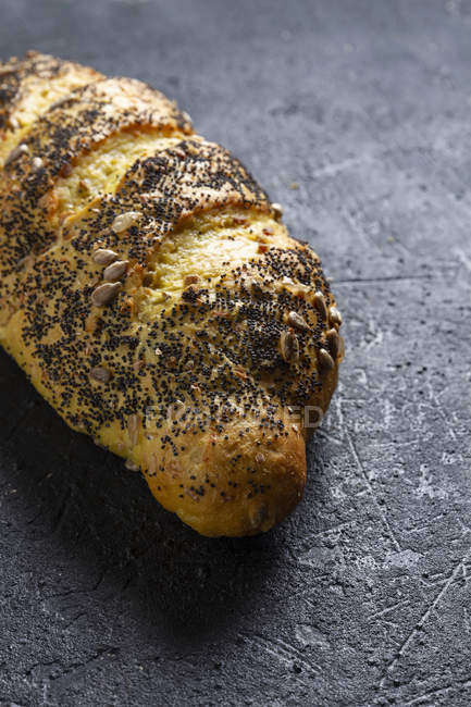 Loaf of ruddy crispy fresh bread with grains and poppy seeds on grey background — Stock Photo