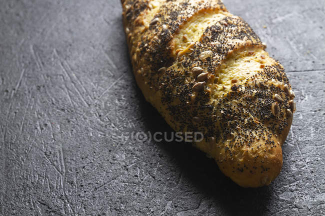 Loaf of ruddy crispy fresh bread with grains and poppy seeds on grey background — Stock Photo