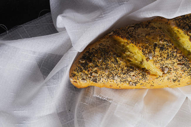 Loaf of baguette bread with grains and poppy seeds on white towel — Stock Photo