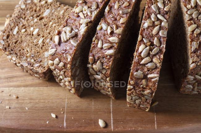 Pane integrale affettato con semi su tagliere di legno — Foto stock