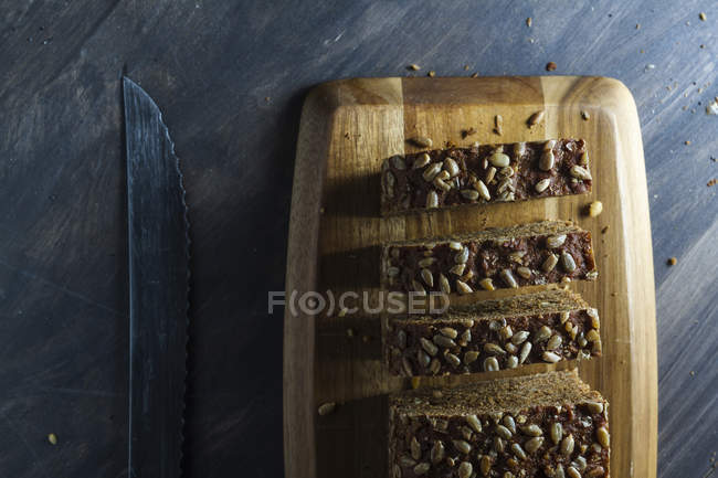 Sliced wholegrain bread with seeds on wooden cutting board — Stock Photo
