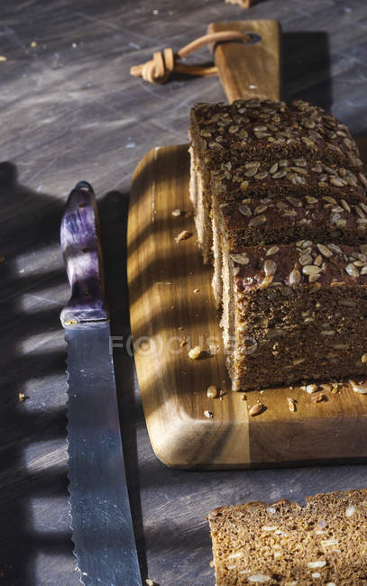 Sliced wholegrain bread with seeds on wooden cutting board — Stock Photo
