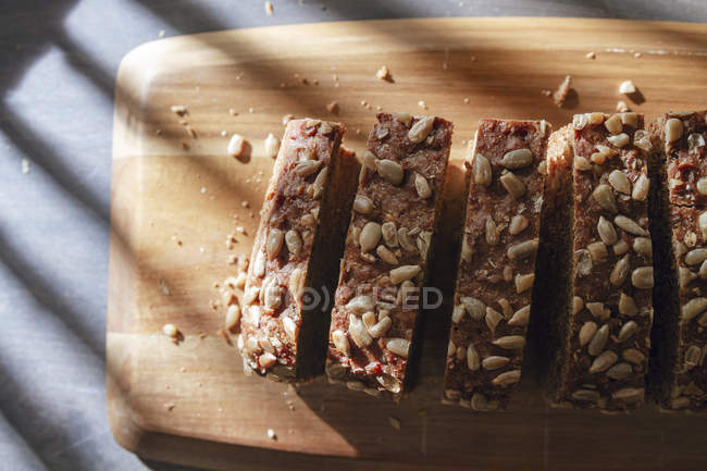 Pan integral en rodajas sobre tabla de cortar de madera sobre mesa con sombra - foto de stock