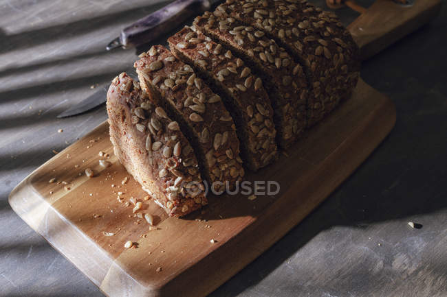 Sliced wholegrain bread on wooden cutting board on table with shadow — Stock Photo