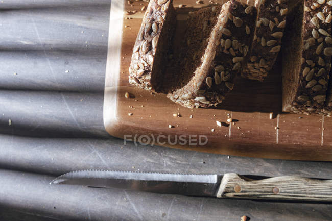 Pão integral fatiado em tábua de corte de madeira na mesa com sombra — Fotografia de Stock