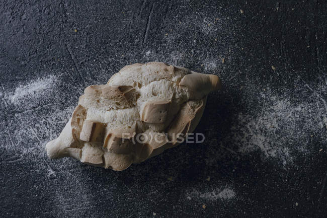 Vista superior de pão artesanal crosty fresco com várias incisões no fundo cinza polvilhado com farinha branca — Fotografia de Stock