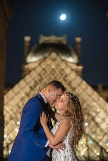 Junges frisch verheiratetes Paar in Hochzeitsanzug und Brautkleid umarmt, während es in einem Schaukelbogen mit Raster im Hintergrund in Paris steht — Stockfoto